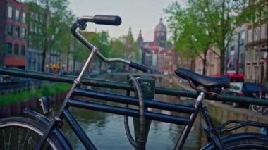 Kanal boyunca turist teknesi, köprüsü ve eski evleri bulunan Amsterdam manzaralı kanalı kuruluyor. İnsanlar bisiklet ve elektrikli tekne kullanıyor..