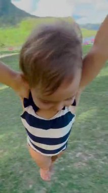 Anne ve kızı birlikte oynuyorlar. Gülen kızı olan genç bir anne, yeşil çimlerde oynaşıyor. Genç anne küçük kızını sallarken eğleniyor..