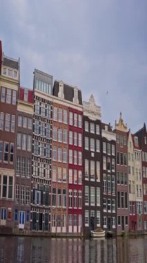 Amsterdam manzaralı bir şehir manzarası, kanal boyunca eski evler kuruyor. Bisiklet süren insanlar.