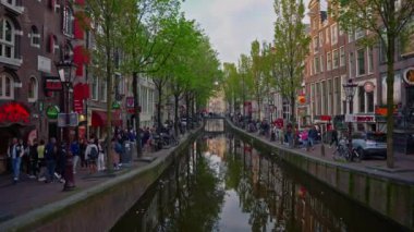 Amsterdam, Hollanda, 09 Haziran 2024: Kanal boyunca eski evler ve geçen turist teknesi ile Amsterdam manzaralı şehir manzaralı kanal kurma. Bisiklet ve elektrik taşımacılığı.