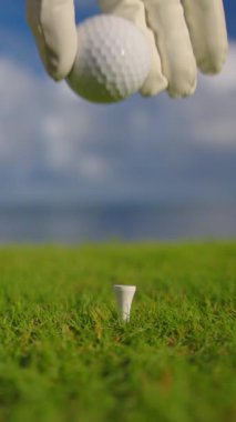 Golfçü golf sahasındaki golf sahasına golf topu koyuyor. Kapatın. Golf eldivenli bir erkek, topu mavi okyanusun arka planındaki sahaya koyar..
