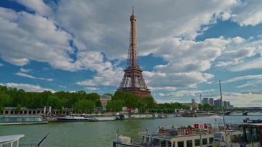 Seine nehri boyunca Eyfel Kulesi 'nin zaman çizelgesi. Uçan tekneler hareket bulanıklığıyla geçiyor. Güneşli ama bulutlu bir bahar günü Paris Şehri nehir kenarı manzaralı köprünün tarihi geçmiş panorama.