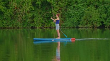 Ayağa kalk ve kürek çek. Sup yönetim kurulu yolculuğu. Sörf yaparken yüzen genç bir kadın. Gün batımında su sporu sörf tahtasında yüzüyor.