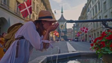 Şapkalı ve sırt çantalı kız turist yazın İsviçre 'nin Bern kentindeki bir çeşmeden su içiyor..