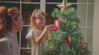 Küçük güzel bir kız, büyü beklentisiyle evinde annesiyle birlikte bir Noel ağacı süsler. Tatil hazırlığı.