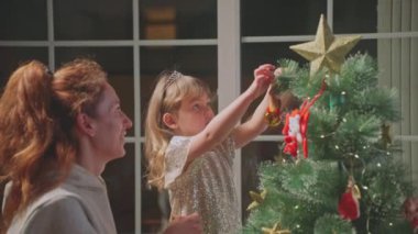 Küçük güzel bir kız, büyü beklentisiyle evinde annesiyle birlikte bir Noel ağacı süsler. Tatil hazırlığı.