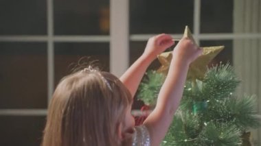 Küçük güzel bir kız sihir beklentisiyle evinde bir Noel ağacı süslüyor. Tatil hazırlığı. Kapat..