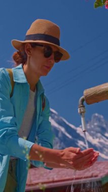 Sırt çantalı bir turist İsviçre 'deki yerel bir çeşmeden su içiyor. Dağların arka planına karşı çok güzel bir yerde elleriyle su topluyor..