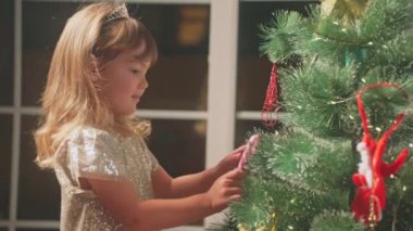 Küçük güzel bir kız sihir beklentisiyle evinde bir Noel ağacı süslüyor. Tatil hazırlığı. Kapatın. Yüksek kalite 4k görüntü