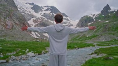 Resimli bir yerde duran genç bir adam Alpler 'in arka planına karşı ellerini kaldırır ve sonsuz bir özgürlük ve neşe hissi gösterir..