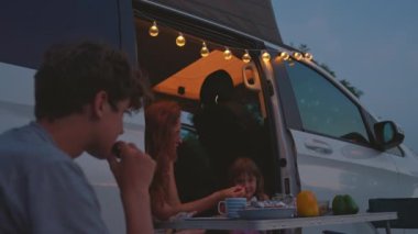 Anne çocuklarla birlikte bir karavanda oturuyor ve dışarıda akşamın tadını çıkarıyor. Bir karavanda aile gezisi.
