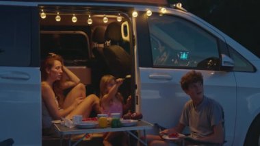 Anne çocuklarla birlikte bir karavanda oturuyor ve dışarıda akşamın tadını çıkarıyor. Bir karavanda aile gezisi.