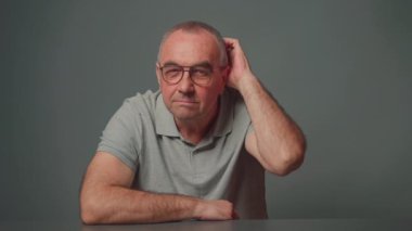 Gri arka planda emekli bir adam cevabını bulduğunu göstermek için kafasını varsayım ve jestlerle kaşıyarak geri bildirim gönderir..