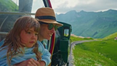 Bir anne ve küçük kızı ünlü kırmızı buharlı trenle İsviçre Alpleri 'ndeki Brienz kasabasından Alp çayırları boyunca yazın dağın zirvesine çıkıyorlar. İsviçre.