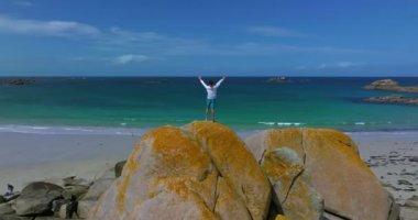 Atlantik Okyanusu kıyısında, Amiets plajında büyük kayaların üzerinde duran genç adam elini kaldırıyor ve Fransa 'nın doğanın güzelliğinin tadını çıkarıyor..