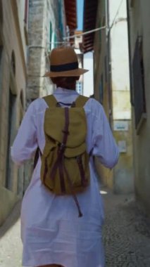 Dikey video. Sırt çantalı genç ve çekici bir turist seyahat ederken eski şehrin sokaklarında geziniyor, mimariye hayran, etrafa bakıyor. İtalya.