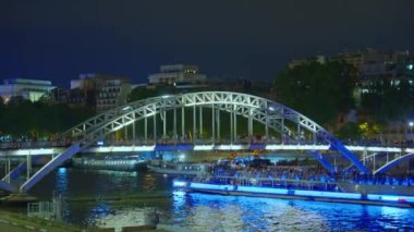 Aydınlatılmış turist teknesi Paris 'te aydınlatılmış bir köprünün altından geçen Seine nehri boyunca ilerliyor..