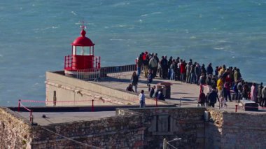 Portekiz, Nazare, 20 Şubat 2025: İnsanlar deniz fenerinde duruyor ve Nazare Portekiz 'in en ünlü yerinde sörfçülerin dev dalgaları fethetmelerini izliyorlar..