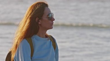 Gün batımında okyanusa yakın gözlüklü bir kızın portresi..