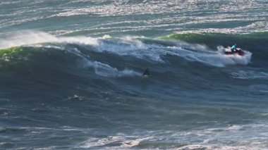 Büyük dalgalar, onları aşırı sporla fethetmeye çalışan bir sörfçüyü taşıyor. Nazare, Portekiz.