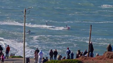 Ayakta duran ve deneyimli sörfçüleri seyreden insanlar büyük dalgalarda sörf yapıyorlar. Nazare, Portekiz, 15 Mart 2025.