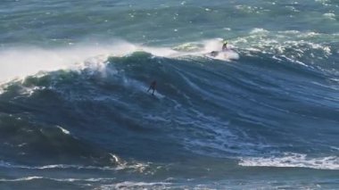 Büyük dalgalar, onları aşırı sporla fethetmeye çalışan bir sörfçüyü taşıyor. Nazare, Portekiz.