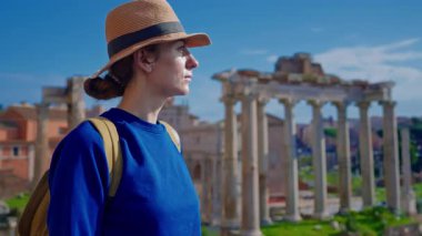 Şapkalı ve sırt çantalı mutlu turist kadın Roma Forumu 'ndaki Antik Roma Sütunları' nın manzaralarını düşünüyor. İtalya.
