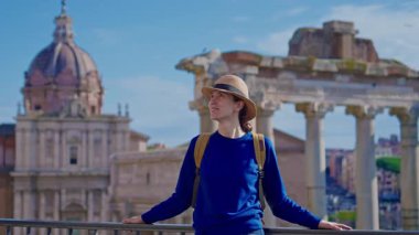 Şapkalı ve sırt çantalı mutlu turist kadın Roma Forumu 'ndaki Antik Roma Sütunları' nın manzaralarını düşünüyor. İtalya.