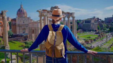 Şapkalı ve sırt çantalı turist kadın Roma Forumu 'ndaki Antik Roma Sütunları' nın manzaralarını düşünüyor. İtalya. Arka planda yürüyen bir kız manzarası manzarası.