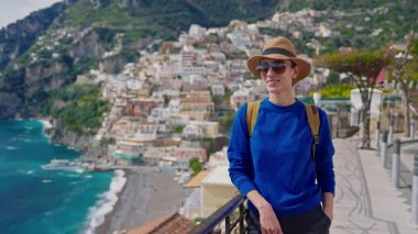 Şapkalı ve sırt çantalı bir kız turist Amalfi kıyısındaki ünlü İtalyan turist kasabası Positano 'nun güzelliğine hayran. İtalya.