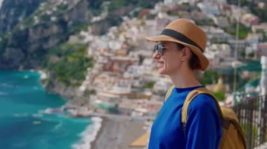 Şapkalı ve sırt çantalı bir kız turist Amalfi kıyısındaki ünlü İtalyan turist kasabası Positano 'nun güzelliğine hayran. İtalya.
