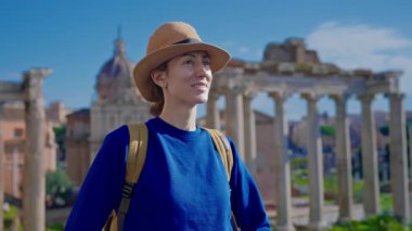 Şapkalı ve sırt çantalı mutlu turist kadın Roma Forumu 'ndaki Antik Roma Sütunları' nın manzaralarını düşünüyor. İtalya.