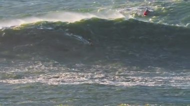 Büyük dalgalar, onları aşırı sporla fethetmeye çalışan bir sörfçüyü taşıyor. Nazare, Portekiz.