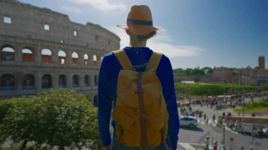 Şapkalı ve sırt çantalı bir kız Roma 'daki Colosseum' un arka planında Roma 'nın ünlü simgesine bakıyor. İtalya.