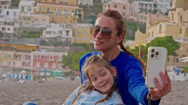 Bir anne ve küçük kızı, İtalya 'nın Amalfi Sahili' ndeki Positano sahilinde otururken selfie ve fotoğraf çekiyorlar. İtalya.
