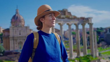 Şapkalı ve sırt çantalı mutlu turist kadın Roma Forumu 'ndaki Antik Roma Sütunları' nın manzaralarını düşünüyor. İtalya.