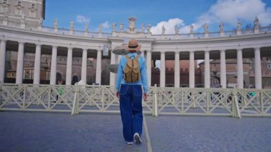 Şapkalı ve sırt çantalı bir kız Vatikan 'daki St. Peters Meydanı' nda yürüyor..