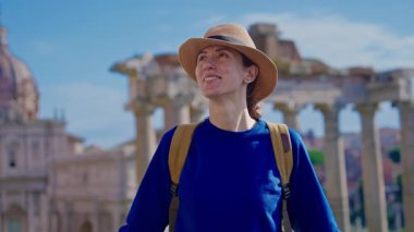 Şapkalı ve sırt çantalı mutlu turist kadın Roma Forumu 'ndaki Antik Roma Sütunları' nın manzaralarını düşünüyor. İtalya.