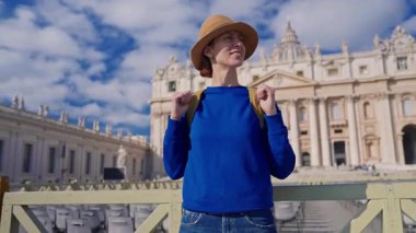 Şapkalı ve sırt çantalı bir turist kız Vatikan 'daki Aziz Peters Bazilikası' nın önünde duruyor..