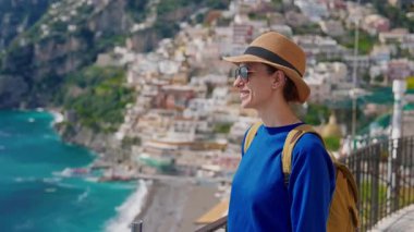 Şapkalı ve sırt çantalı bir kız turist Amalfi kıyısındaki ünlü İtalyan turist kasabası Positano 'nun güzelliğine hayran. İtalya.