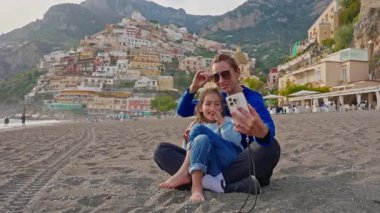 Bir anne ve küçük kızı, İtalya 'nın Amalfi Sahili' ndeki Positano sahilinde otururken selfie ve fotoğraf çekiyorlar. İtalya.