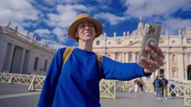 Şapkalı ve sırt çantalı bir turist kız Vatikan 'daki Aziz Peters Bazilikası' nın zemininde telefonuyla selfie çekiyor..