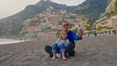 Bir anne ve küçük kızı, İtalya 'nın Amalfi Sahili' ndeki Positano sahilinde otururken selfie ve fotoğraf çekiyorlar. İtalya.
