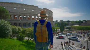 Şapkalı ve sırt çantalı bir kız Roma 'daki Colosseum' un arka planında Roma 'nın ünlü simgesine bakıyor. İtalya.