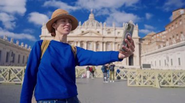 Şapkalı ve sırt çantalı bir turist kız Vatikan 'daki Aziz Peters Bazilikası' nın zemininde telefonuyla selfie çekiyor..