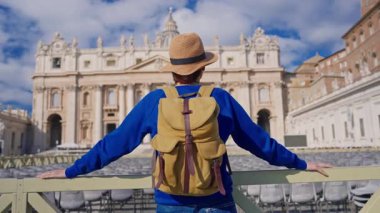 Şapkalı ve sırt çantalı bir turist kız Vatikan 'daki Aziz Peters Bazilikası' nın önünde duruyor..