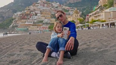 Bir anne ve küçük kızı, İtalya 'nın Amalfi Sahili' ndeki Positano sahilinde otururken selfie ve fotoğraf çekiyorlar. İtalya.
