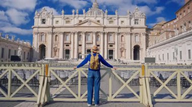 Şapkalı ve sırt çantalı bir turist kız Vatikan 'daki Aziz Peters Bazilikası' nın önünde duruyor..