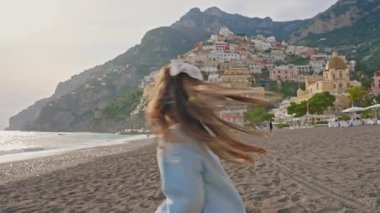 Positano sahilinde koşup gülen tatlı bir kız. Sahilden şehrin ana kısmına, dağdaki renkli evlere bakın. Positano, İtalya.