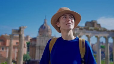 Şapkalı ve sırt çantalı mutlu turist kadın Roma Forumu 'ndaki Antik Roma Sütunları' nın manzaralarını düşünüyor. İtalya.